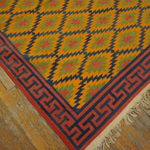 Orange, blue, red, and green serrated diamond flatweave rug with a thick Greek key border on wood floor.