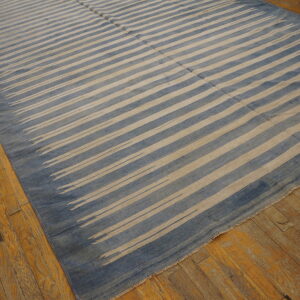 Blue and beige flatwoven rug with striped pattern rests on worn yellow-toned hardwood planks.