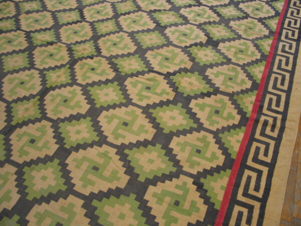 Flat-woven rug featuring tan, light green, and dark gray stepped diamonds and a striped greek key border.