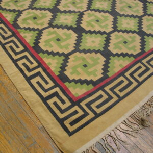 Tan, green, and black flatweave rug featuring a geometric lattice pattern and a Greek key border on wood flooring.