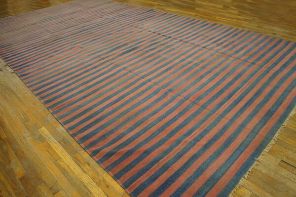 A large blue and faded reddish-pink striped rug covers the worn, light hardwood floor.