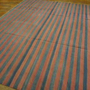 A flatweave rug with wide vertical stripes in faded blue and reddish-pink covers a wood floor.