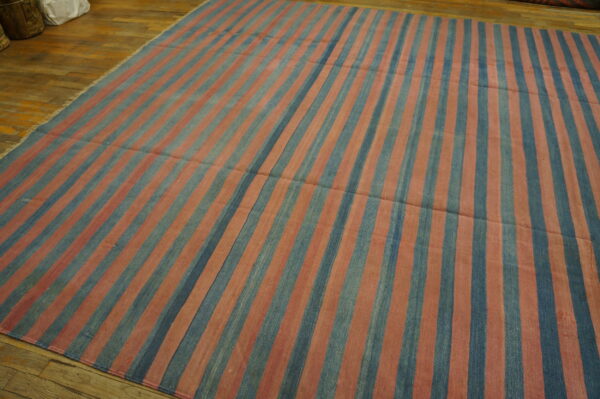 A flatweave rug with wide vertical stripes in faded blue and reddish-pink covers a wood floor.