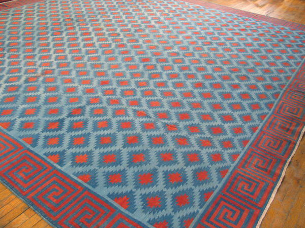 Low-pile blue and orange geometric rug with a thick greek key border on wood flooring.
