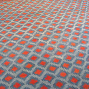 Blue and gray rug with repeating orange diamond motifs and a visible red geometric border on wood.