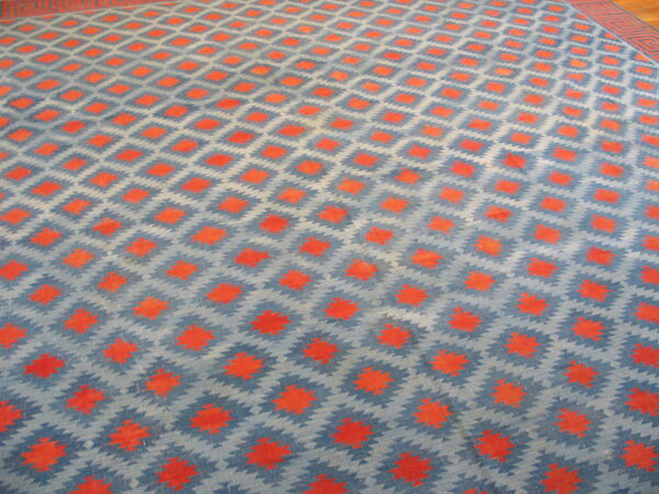 Blue and gray rug with repeating orange diamond motifs and a visible red geometric border on wood.