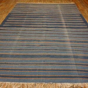 Flatweave blue rug with orange horizontal stripes and fringe covers a distressed wood floor.