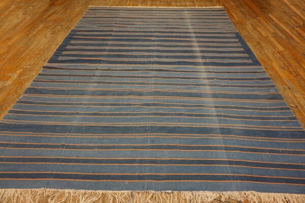 Flatweave blue rug with orange horizontal stripes and fringe covers a distressed wood floor.