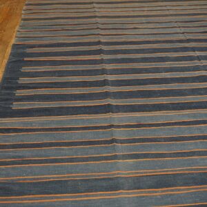Navy, slate blue, and orange striped flatweave rug sits on worn wood plank flooring.