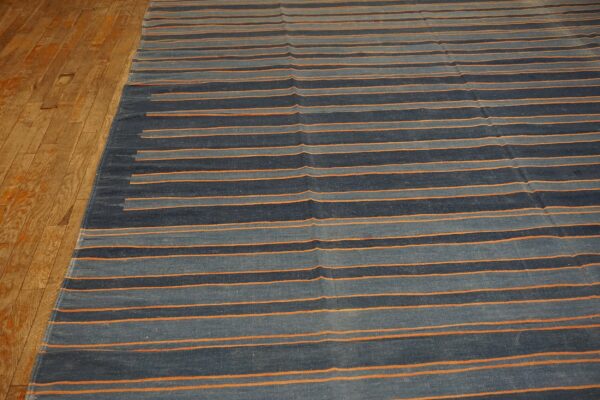Navy, slate blue, and orange striped flatweave rug sits on worn wood plank flooring.