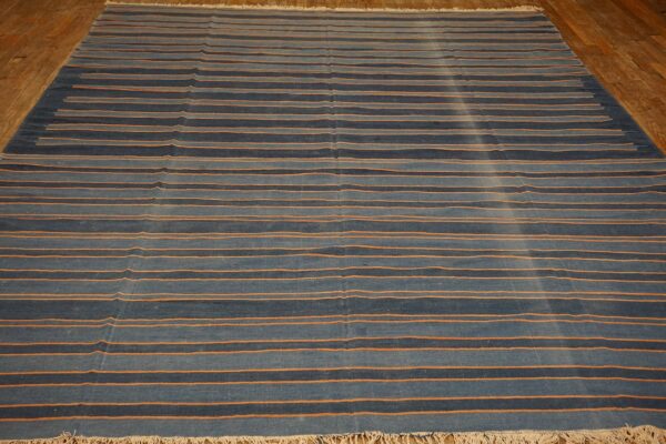 Striped blue rug with contrasting thin orange horizontal lines rests on light brown hardwood flooring.