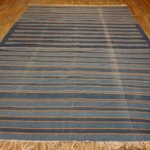Low-pile rug with alternating shades of blue and thin orange stripes rests on a wood floor.