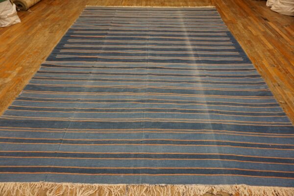 Low-pile rug with alternating shades of blue and thin orange stripes rests on a wood floor.
