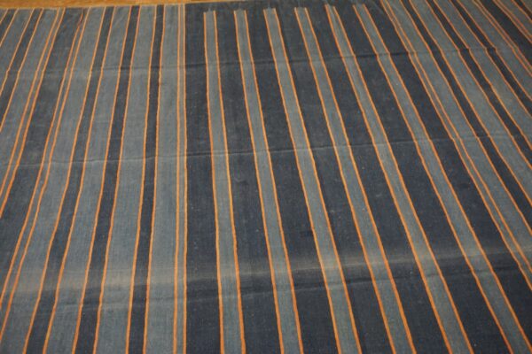 Dark blue and grey striped rug with thin orange accents lying on a wood floor.