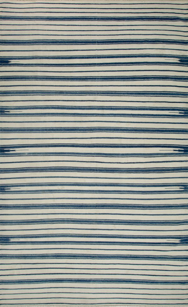Flatweave rug with thick horizontal navy blue and cream stripes, seen over a dark wood floor.