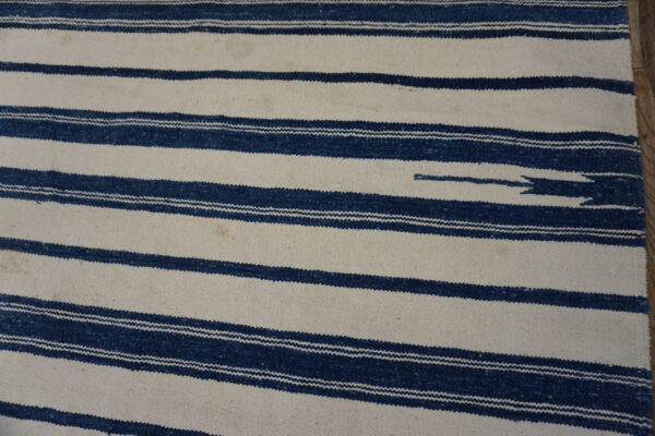 Flatweave rug with thick horizontal navy blue and cream stripes, seen over a dark wood floor.