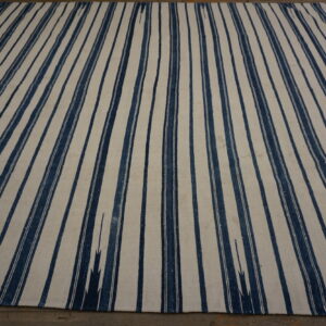 Flat-woven rug featuring wide vertical stripes in indigo blue and creamy white on a dark floor.