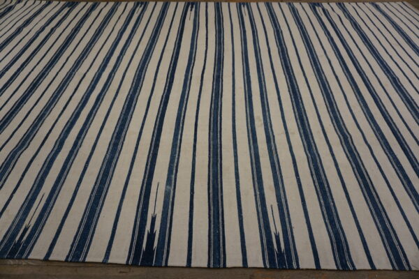 Flat-woven rug featuring wide vertical stripes in indigo blue and creamy white on a dark floor.