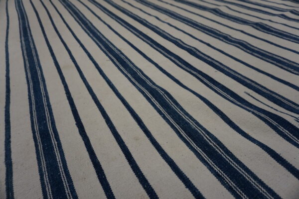 Textured cream rug with wide and narrow repeating dark blue vertical stripes.