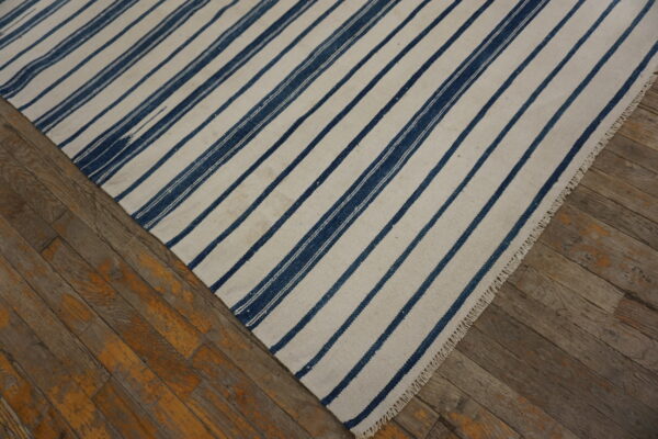 Cream and indigo striped flatweave rug displayed on distressed brown wood flooring.