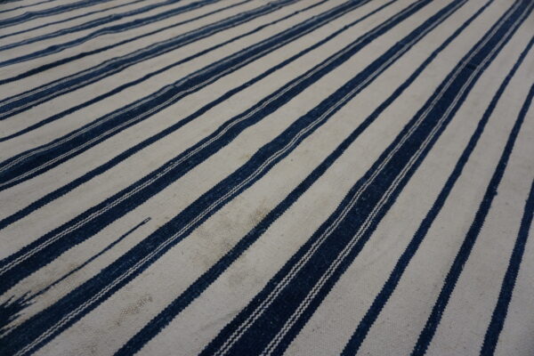 Textured low-pile rug displaying wide cream bands alternating with narrow dark blue vertical stripes.