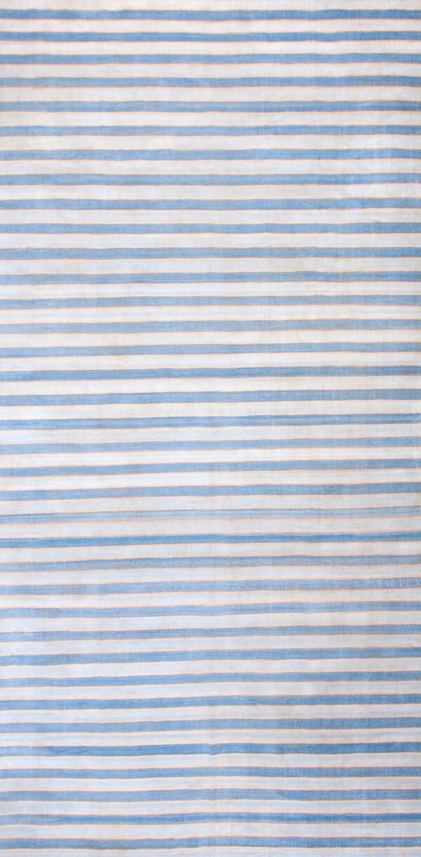 Flatweave rug with alternating blue-gray and beige vertical stripes on a worn hardwood floor.