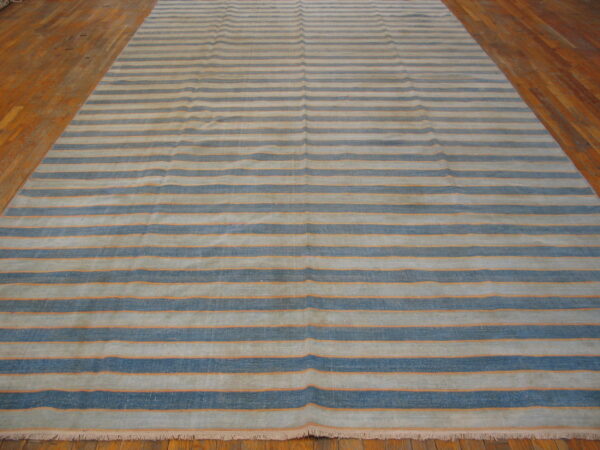 A large rug with alternating light and dark blue horizontal stripes framed by thin orange lines on a wood floor.