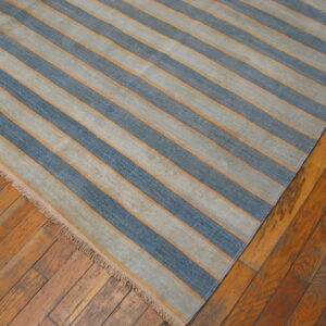 Blue and gray striped flatweave rug with orange details rests on rustic wood floorboards.