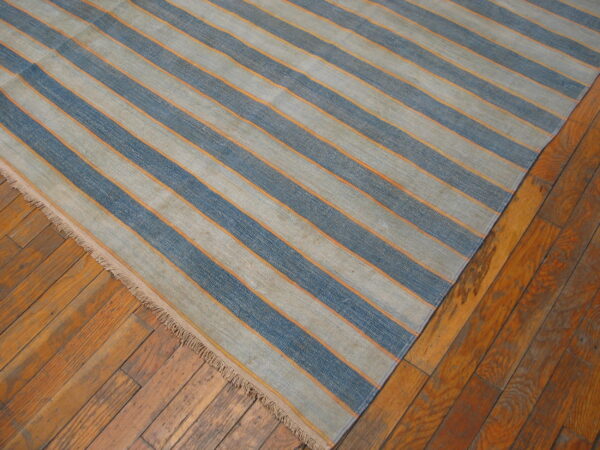 Blue and gray striped flatweave rug with orange details rests on rustic wood floorboards.
