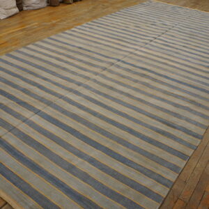 Rectangular flatweave rug featuring blue and beige stripes separated by thin gold lines on a wood floor.