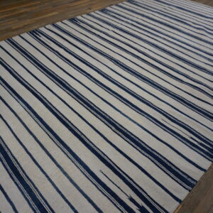Navy and off-white striped flatweave rug displayed on rustic wooden plank flooring.