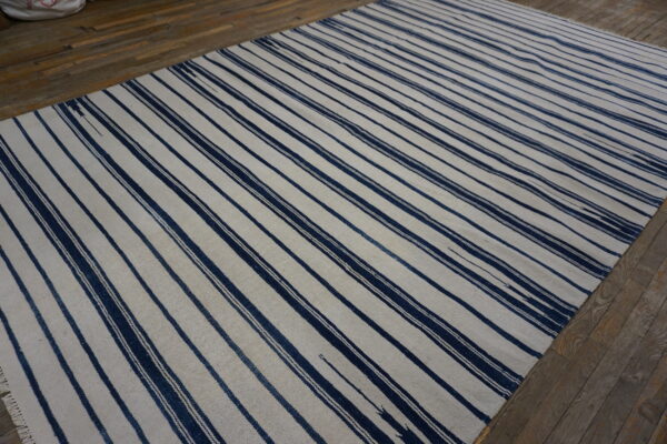 Navy and off-white striped flatweave rug displayed on rustic wooden plank flooring.