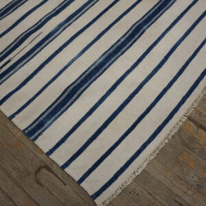 A cream rug with broad dark blue stripes and fringe rests on rustic wood plank flooring.
