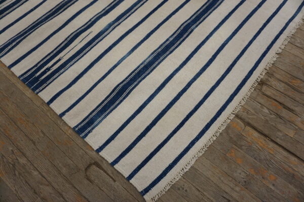A cream rug with broad dark blue stripes and fringe rests on rustic wood plank flooring.