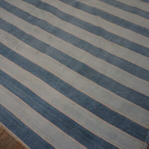 Flatwoven rug in wide diagonal stripes of blue and light gray rests on rustic dark wood planks.