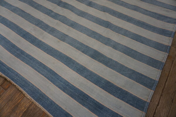 Flatwoven rug in wide diagonal stripes of blue and light gray rests on rustic dark wood planks.