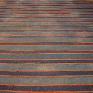 A flatweave rug features wide horizontal stripes in mottled blue and navy, separated by narrow orange lines on a wood floor.