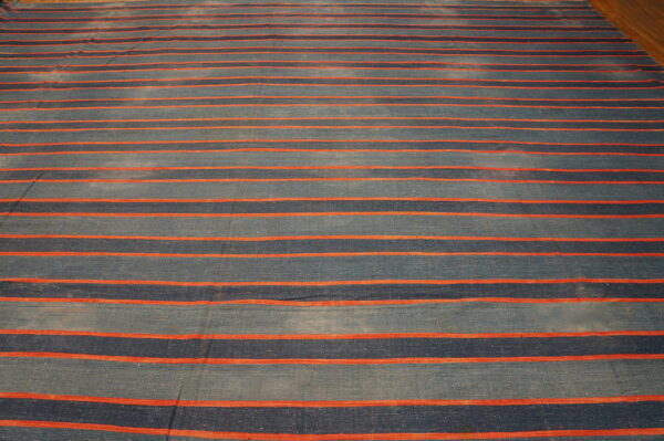 A flatweave rug features wide horizontal stripes in mottled blue and navy, separated by narrow orange lines on a wood floor.