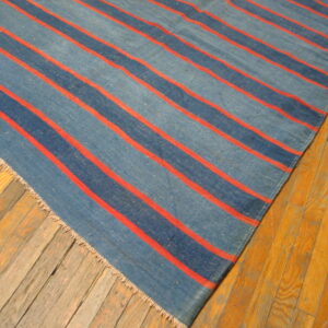 Blue striped flatweave rug with thin orange lines lies diagonally on a distressed light wood floor.