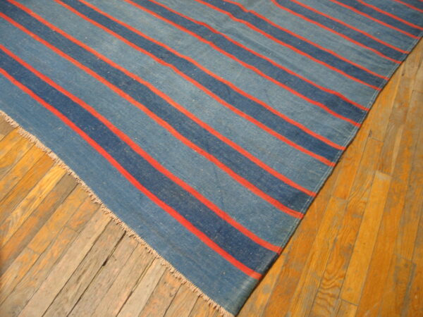 Blue striped flatweave rug with thin orange lines lies diagonally on a distressed light wood floor.