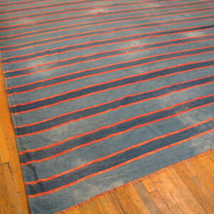 Flatweave rug with thick and thin blue and bright orange horizontal stripes on wood planks.