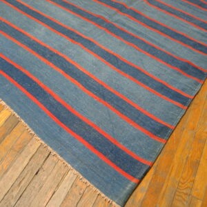 Low-pile rug with wide denim blue stripes and narrow coral red stripes on aged wood flooring.