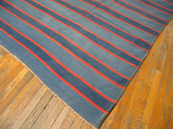 Low-pile rug with wide denim blue stripes and narrow coral red stripes on aged wood flooring.