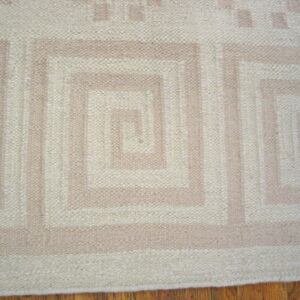 Cream and tan low-profile rug featuring a repeating geometric spiral design on a wood floor.
