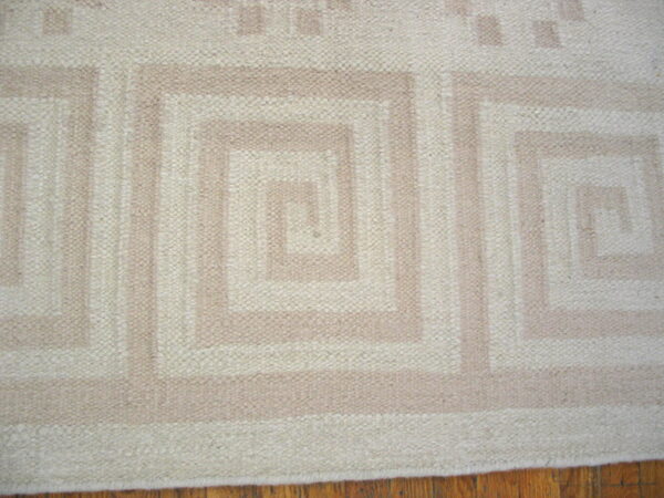 Cream and tan low-profile rug featuring a repeating geometric spiral design on a wood floor.