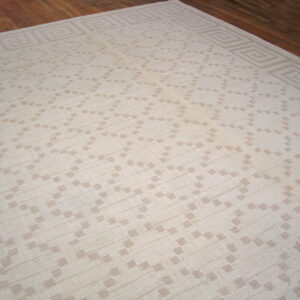 A cream and tan flatwoven rug featuring a geometric pattern and a Greek key border on wood flooring.