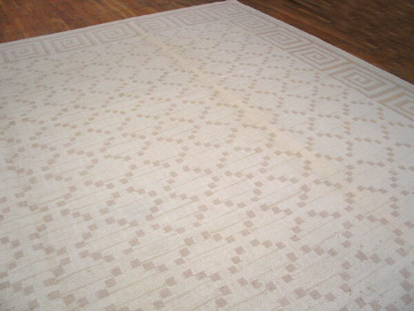 A cream and tan flatwoven rug featuring a geometric pattern and a greek key border on wood flooring.