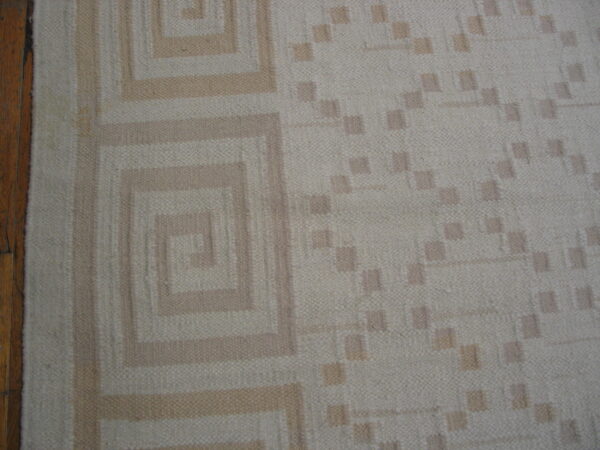 A low-pile beige rug featuring tan concentric squares and square dots rests beside brown wood flooring.