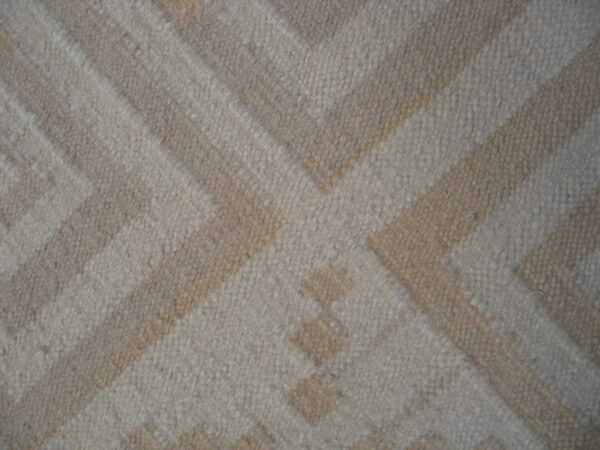 Geometric rug texture showing a large interlocking pattern in contrasting light beige and ivory tones.