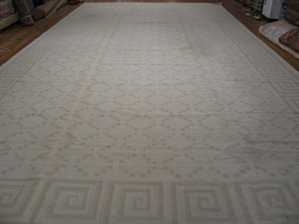 Monochromatic beige rug featuring an overall scattered geometric design and a greek key motif border.